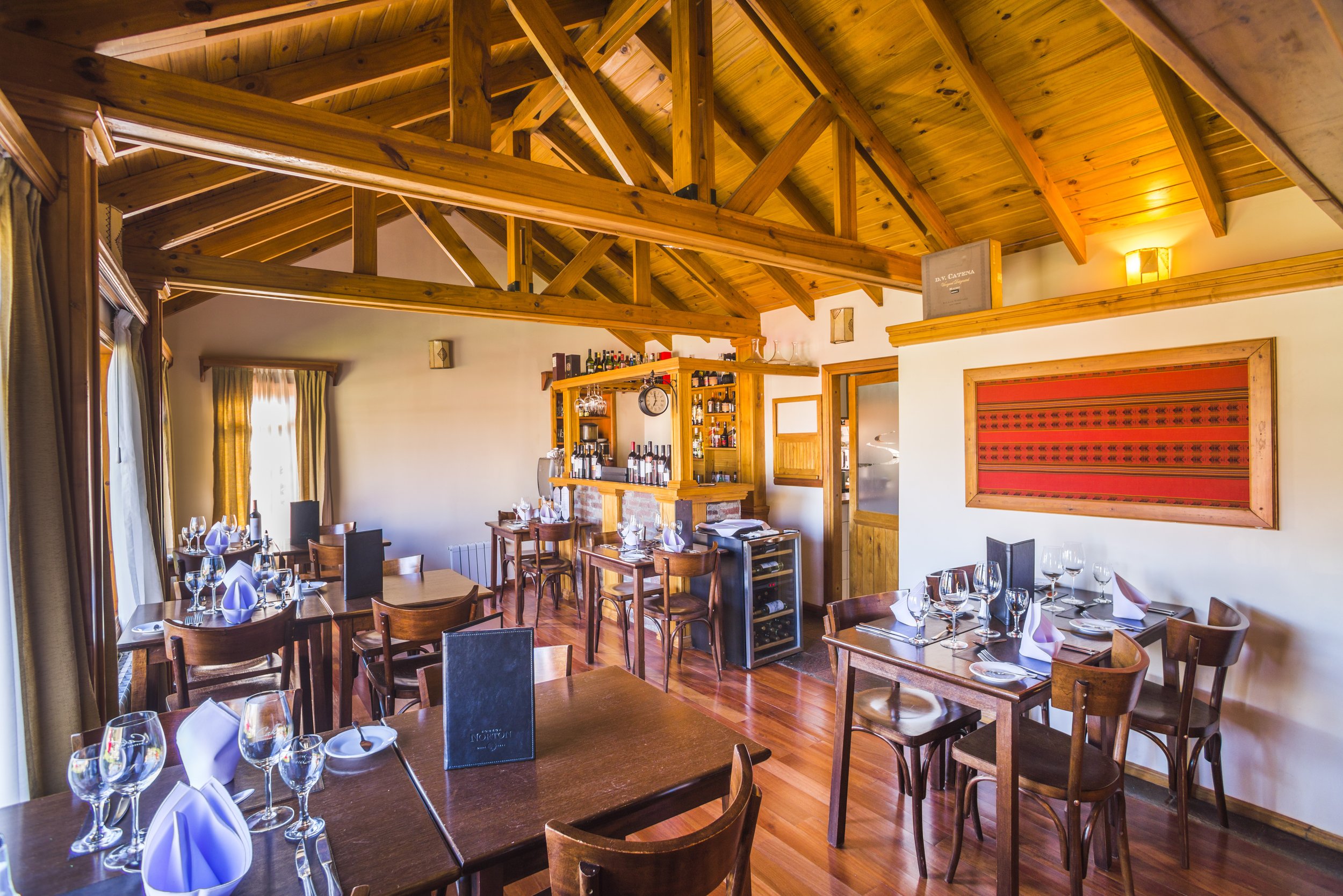 Salón comedor de una hostería con mesas preparadas, techo de madera a dos aguas y una pequeña barra.