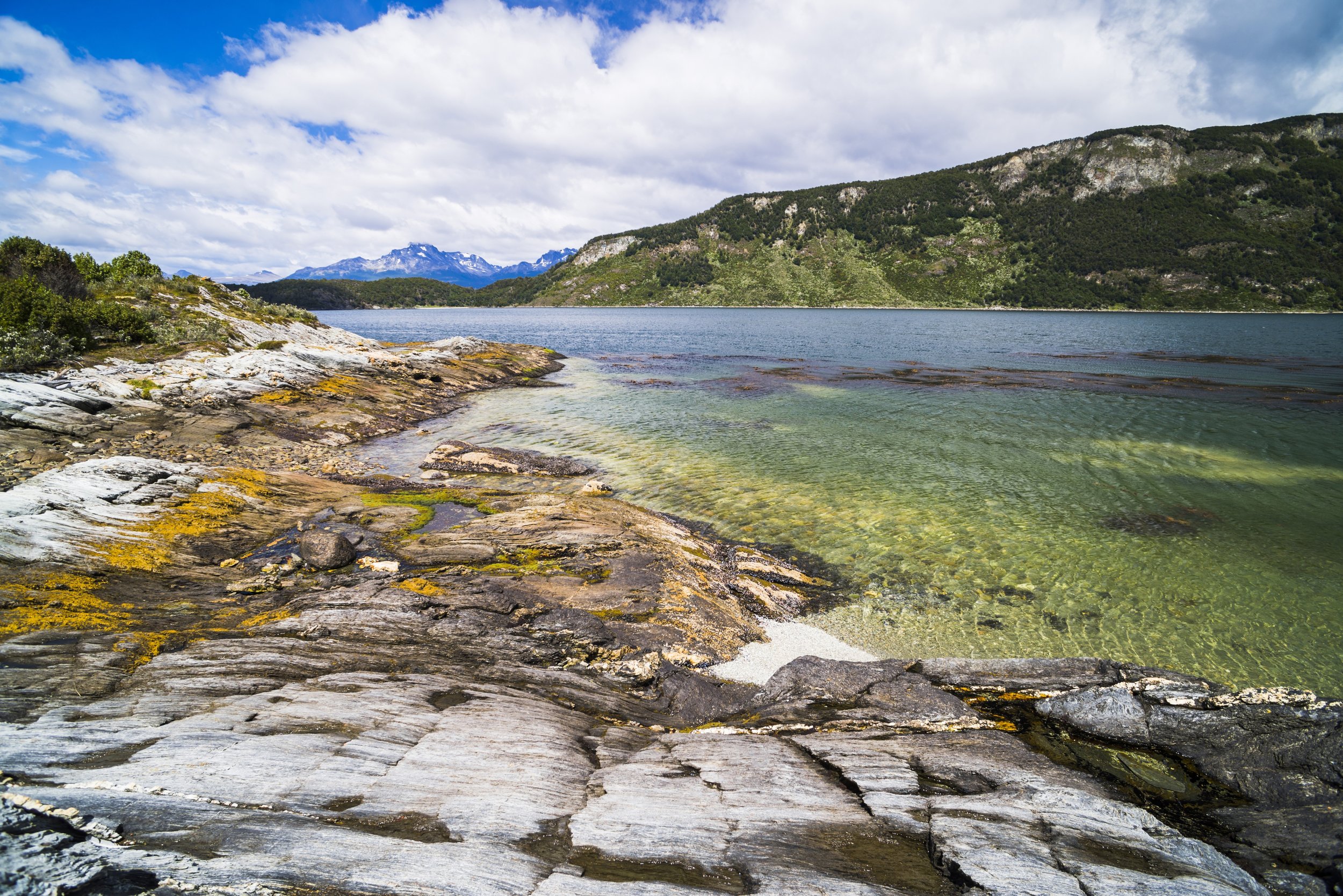 Costa rocosa con aguas claras y montañas de fondo en el Parque Nacional Tierra del Fuego.