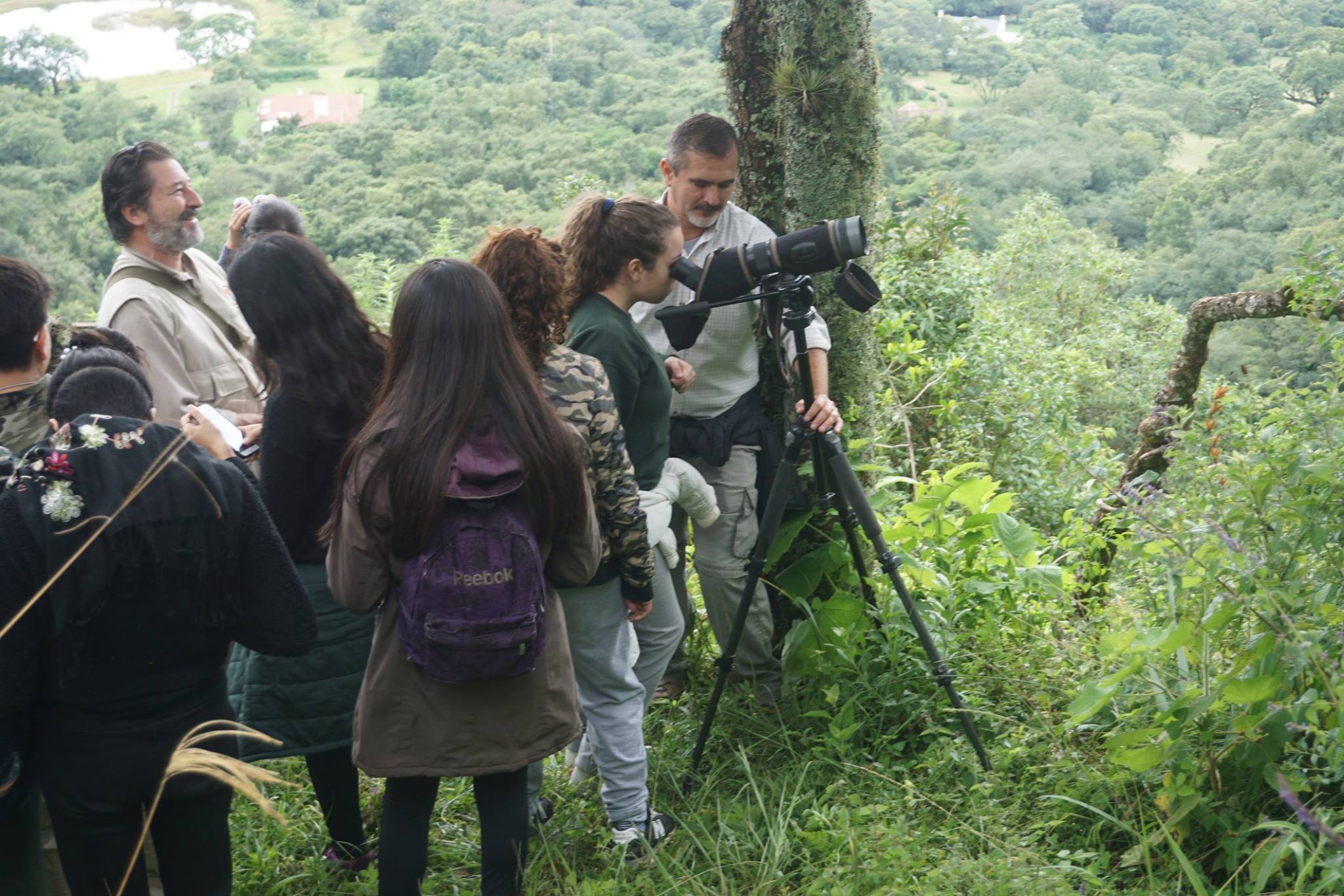 Un grupo de personas realiza observación de aves o fauna con un telescopio terrestre en un entorno boscoso.