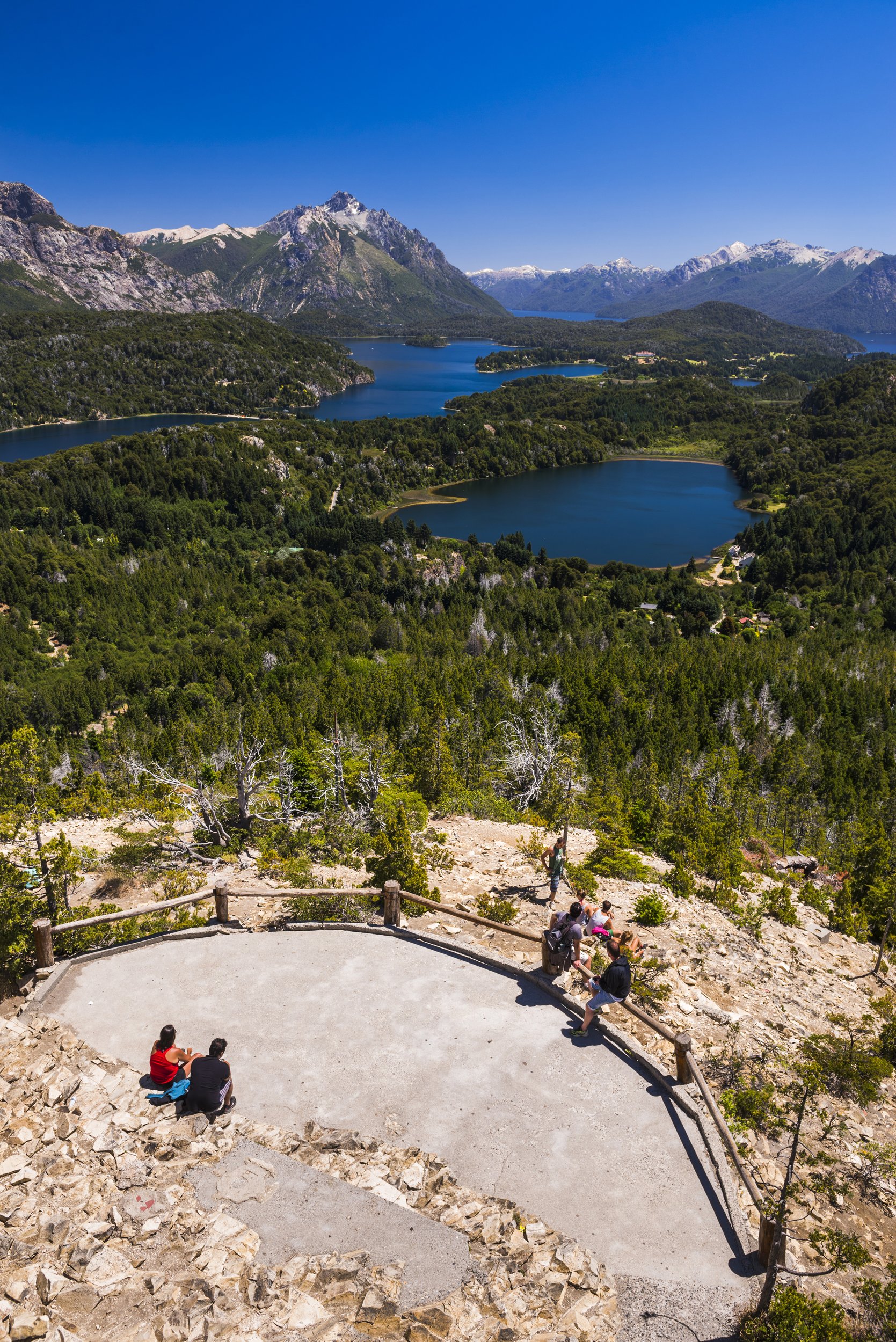 Vista panorámica de lagos, bosques y montañas de Bariloche desde el mirador del Cerro Campanario con turistas.