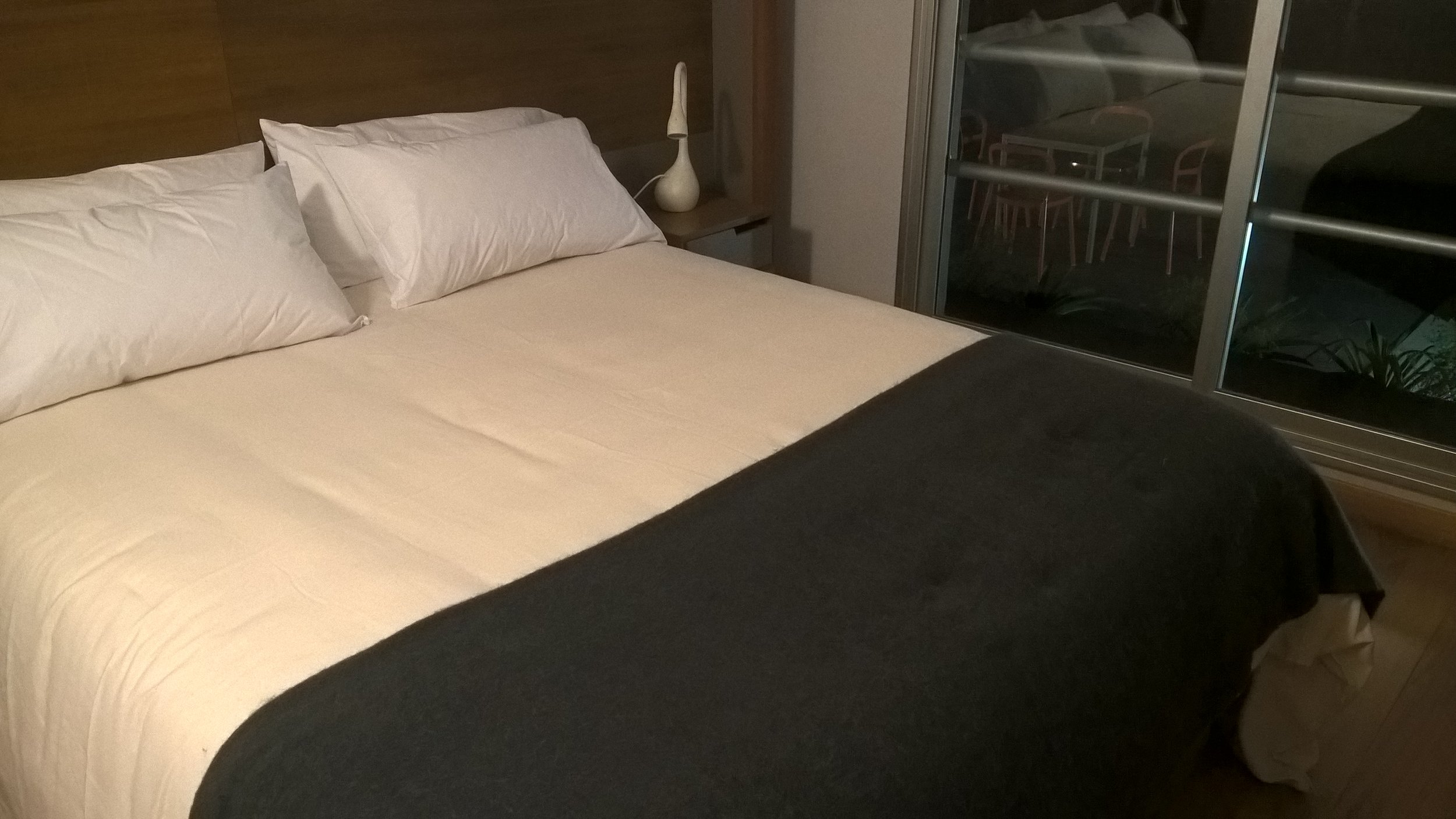 Cama doble tendida en una habitación de hotel con ventanal que da al exterior de noche.