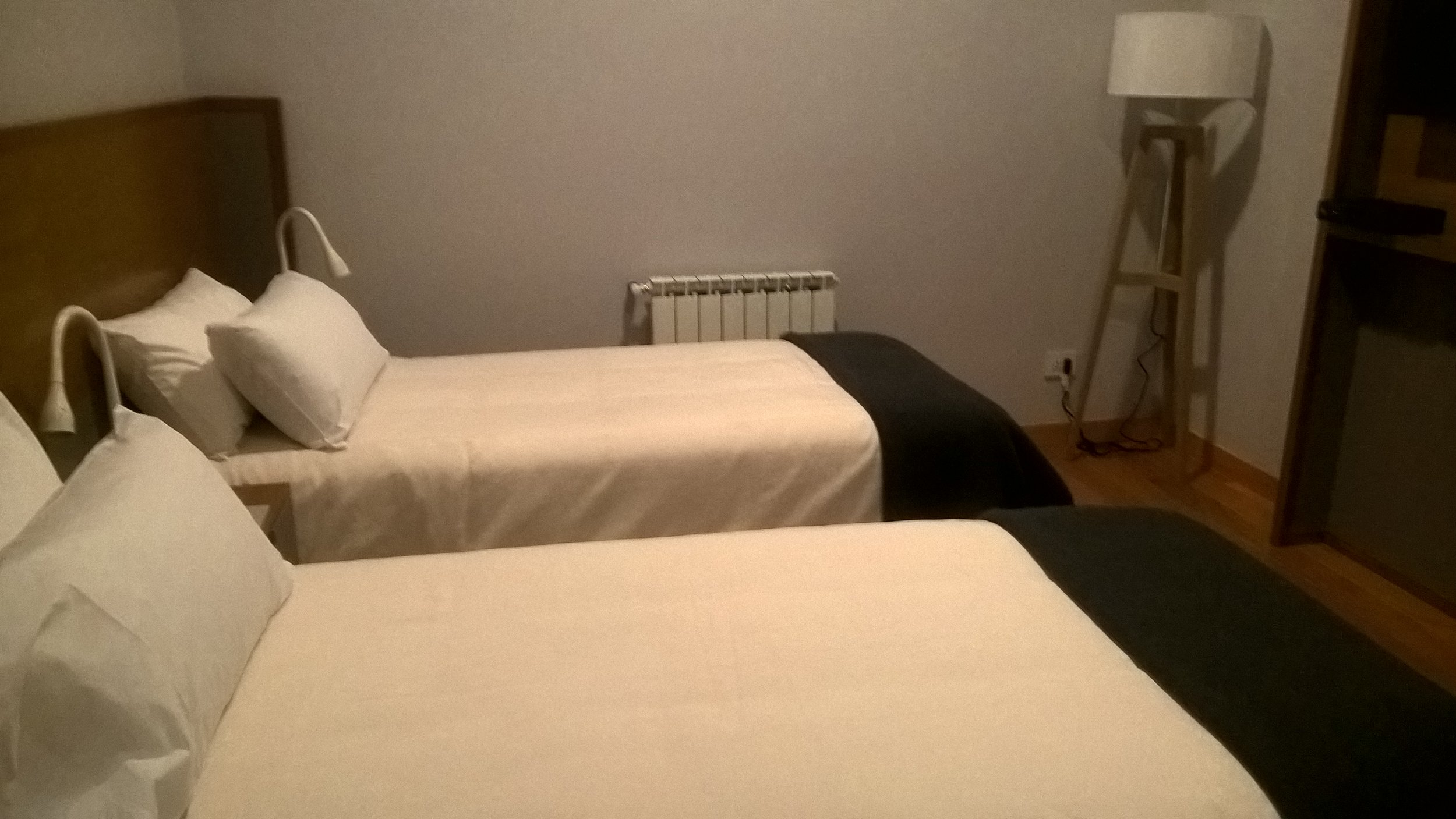 Habitación de hotel con dos camas individuales preparadas con sábanas blancas y lámpara de pie en la esquina.