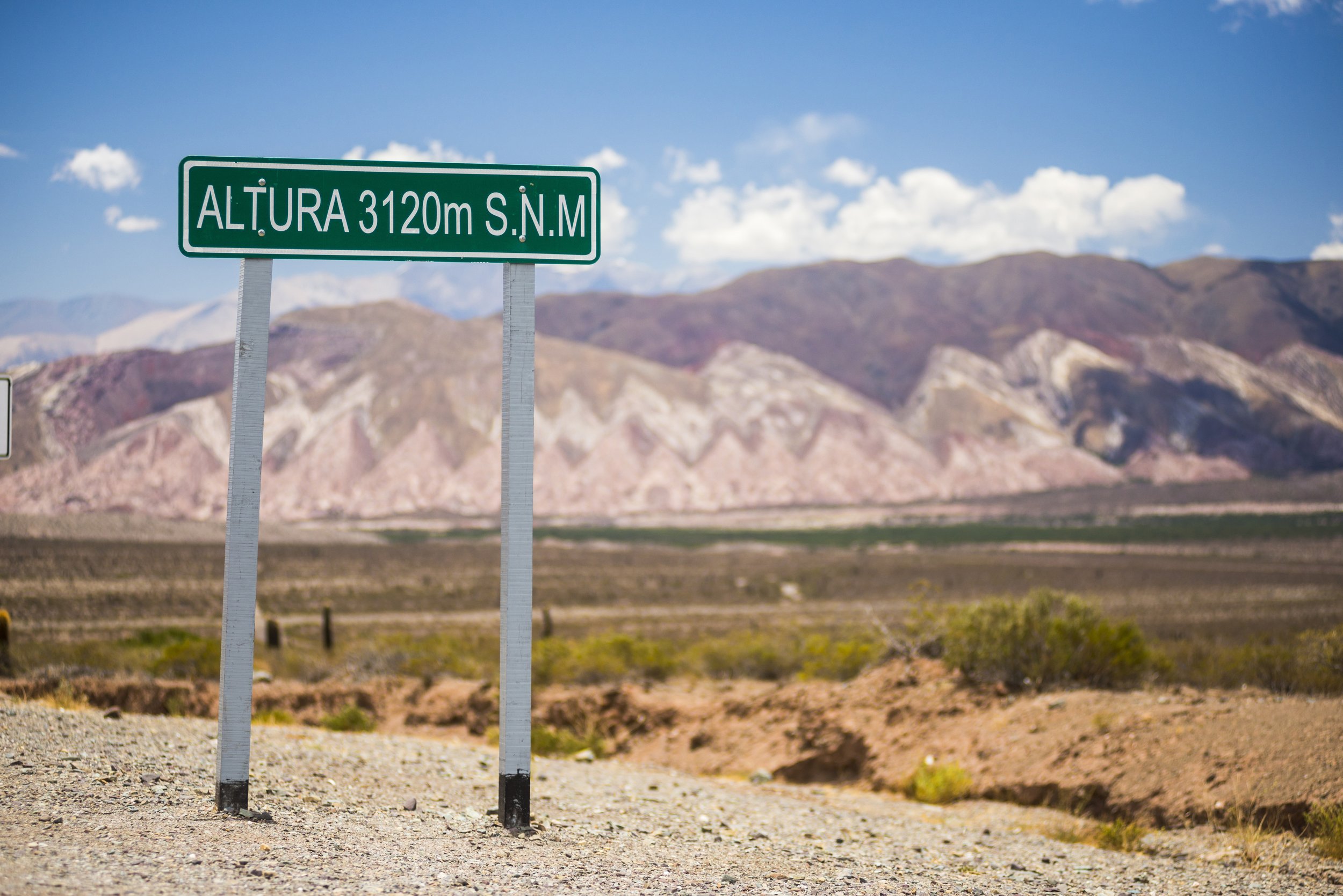 Cartel vial señalando altura sobre el nivel del mar con paisaje árido y cerros coloridos de fondo.
