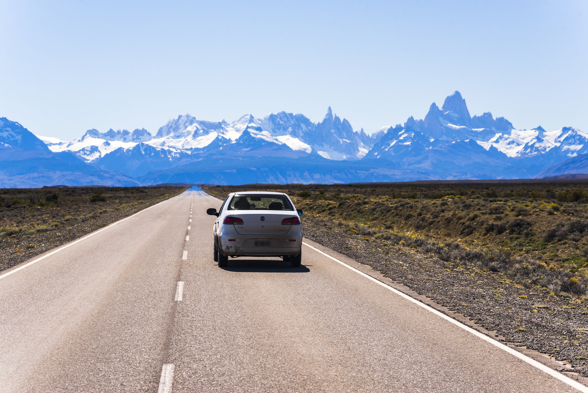 Automóvil circulando por una ruta recta hacia el macizo del Cerro Fitz Roy cubierto de nieve.