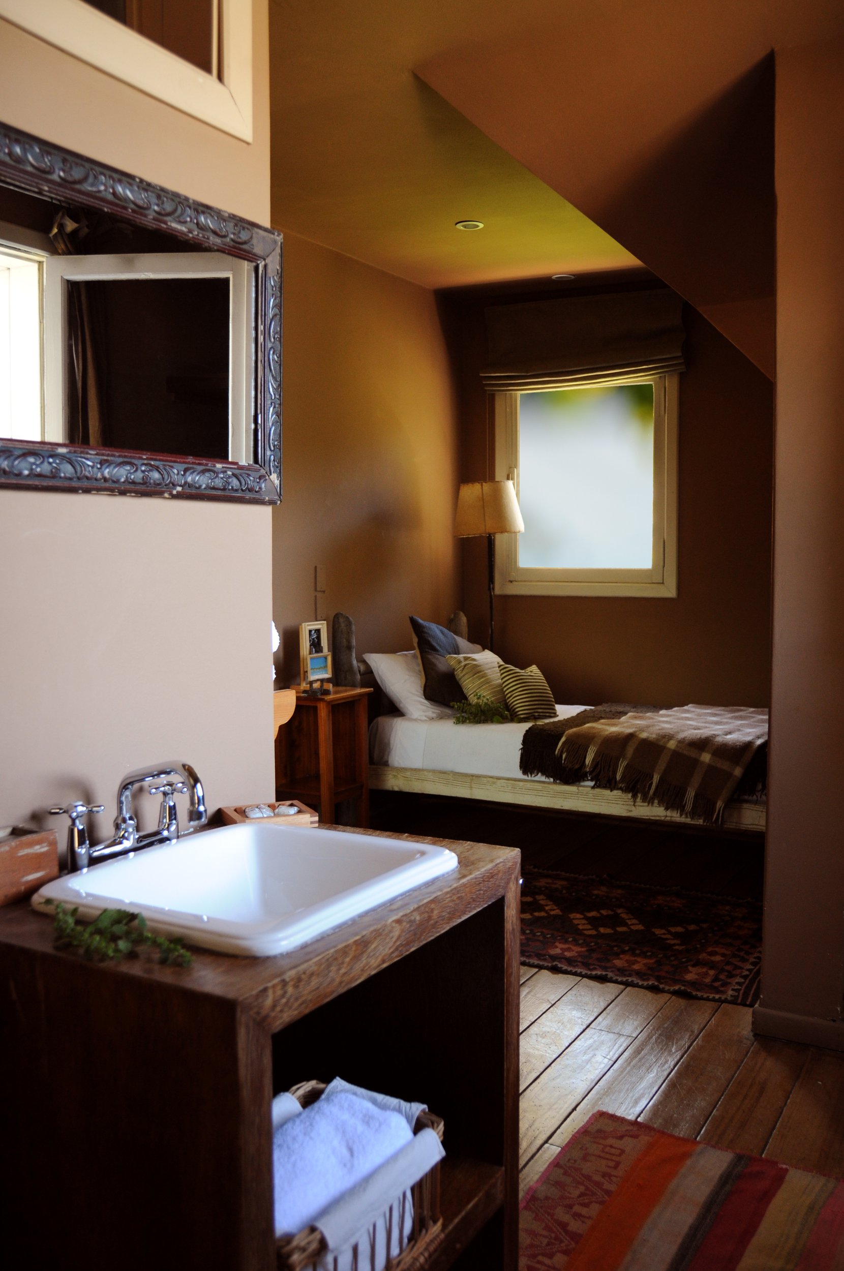 Interior de una habitación de posada con lavamanos de madera en primer plano y cama individual al fondo.