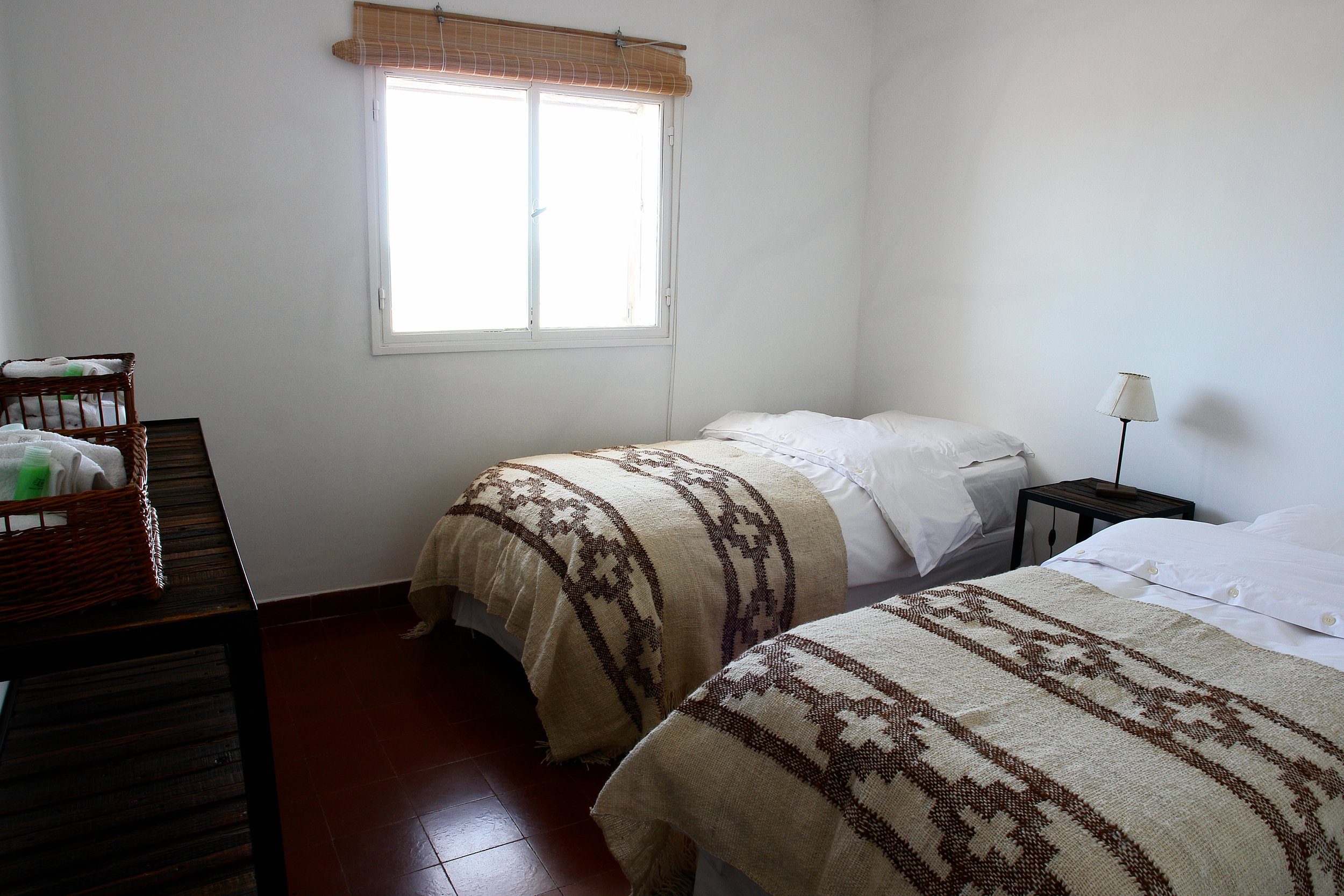 Habitación luminosa con dos camas individuales decoradas con mantas tejidas artesanales y una ventana al fondo.