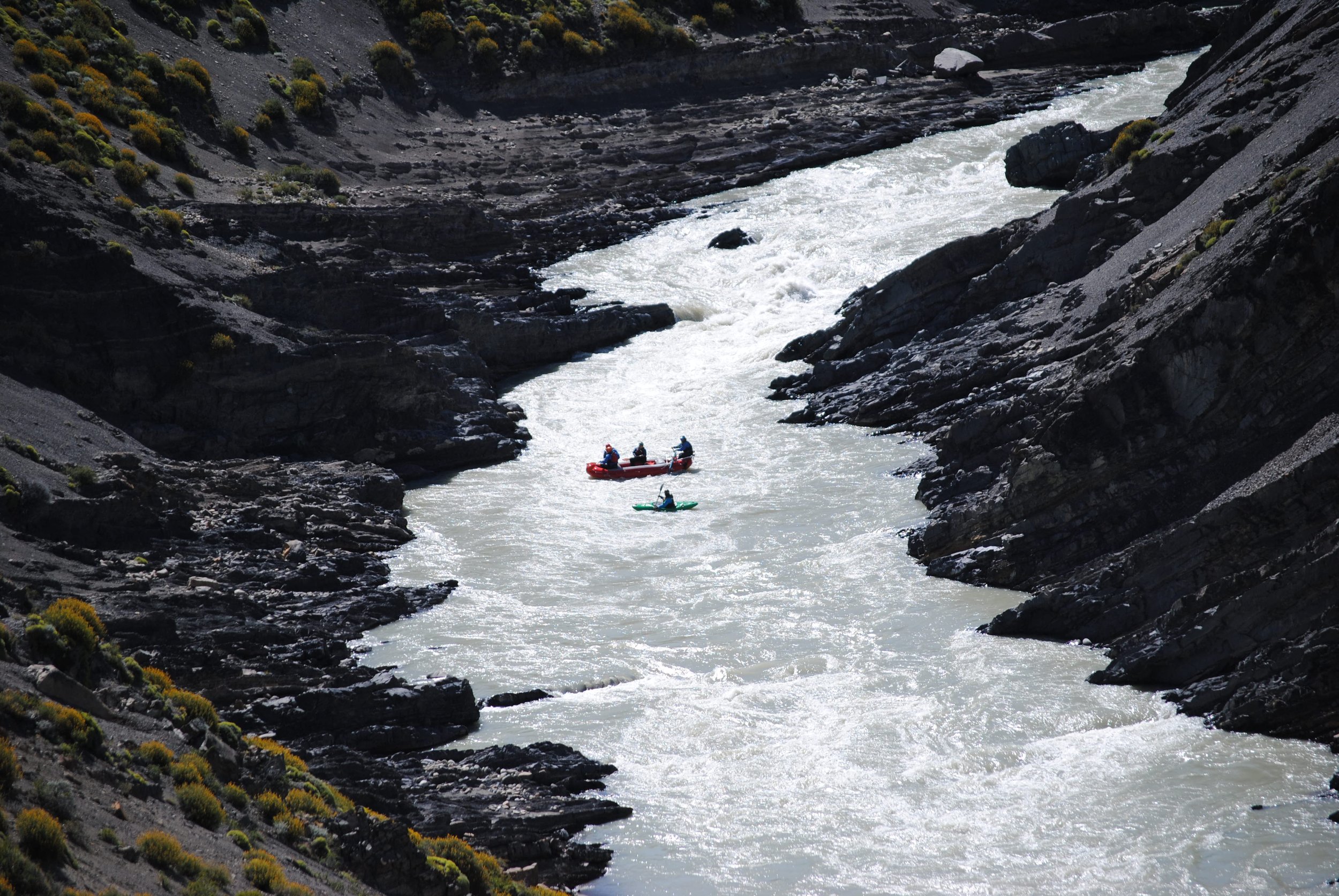 Gente realizando rafting y kayak en un río encajonado entre laderas rocosas en El Chaltén.