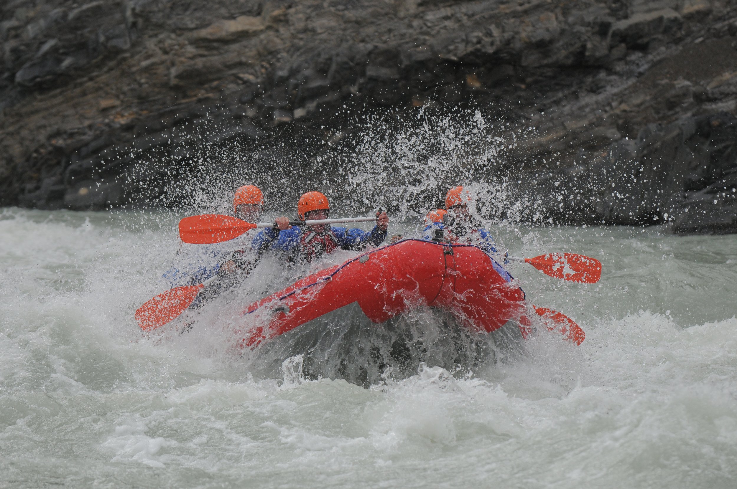 Un grupo de personas navega en un bote de rafting naranja sobre rápidos de aguas blancas.