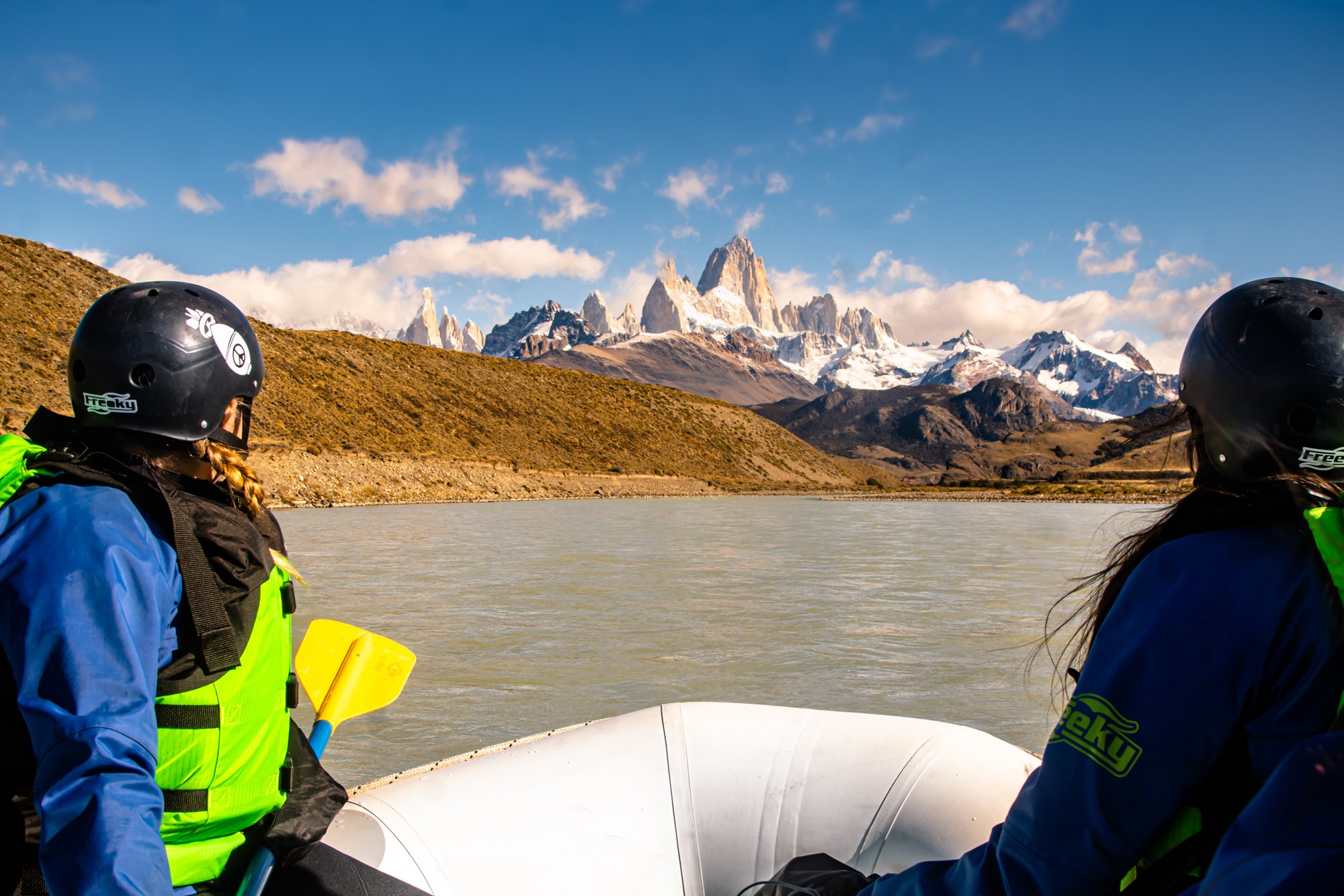 Personas practicando rafting en un río con vista panorámica hacia el Cerro Fitz Roy y la cordillera.