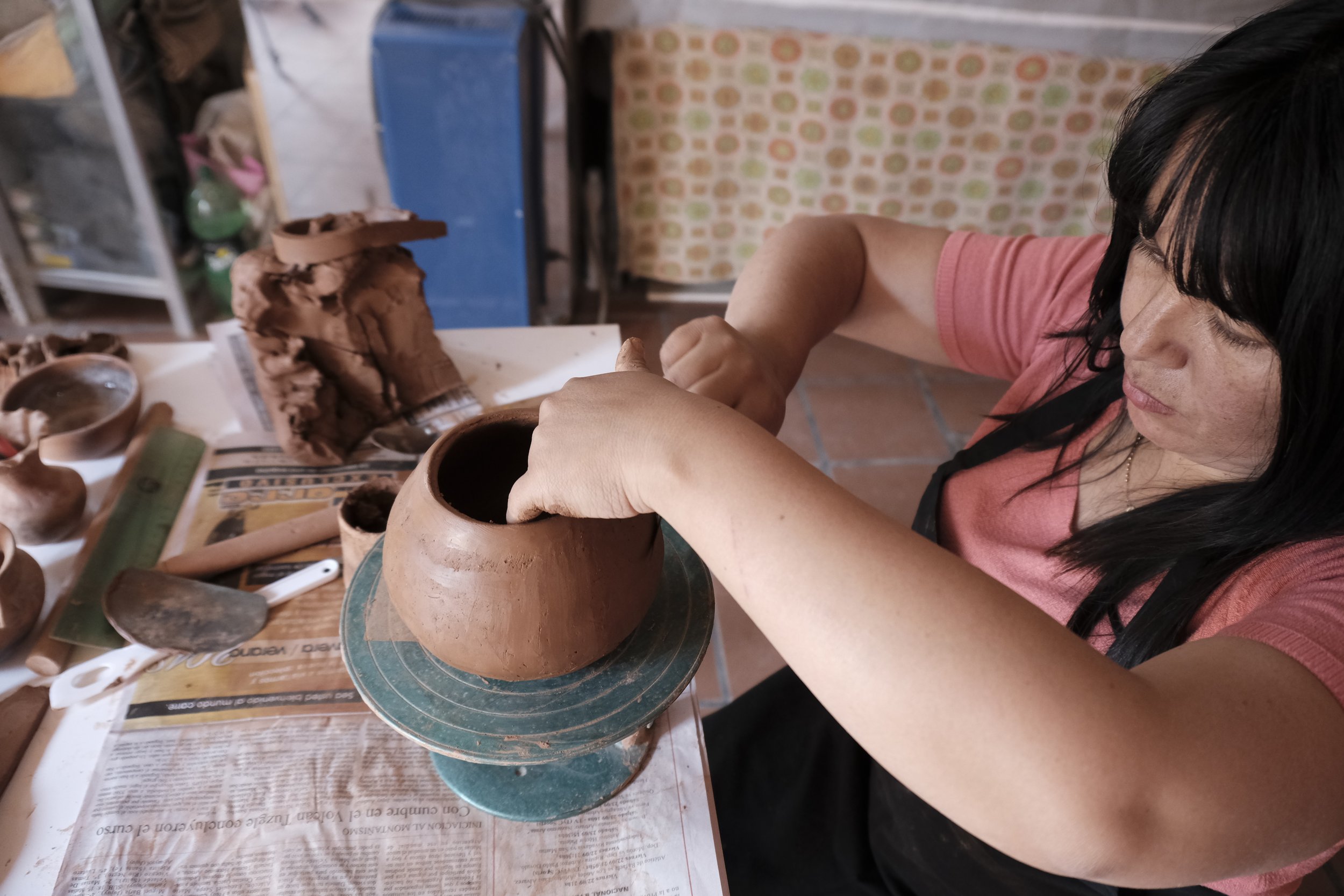 Una mujer moldea una vasija de arcilla con sus manos durante un taller de alfarería artesanal.