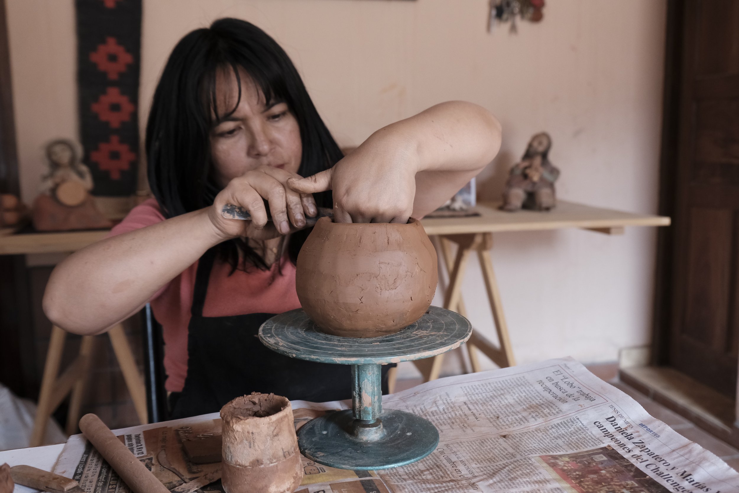Una mujer modela una vasija de arcilla a mano sobre un torno manual en un taller de cerámica.