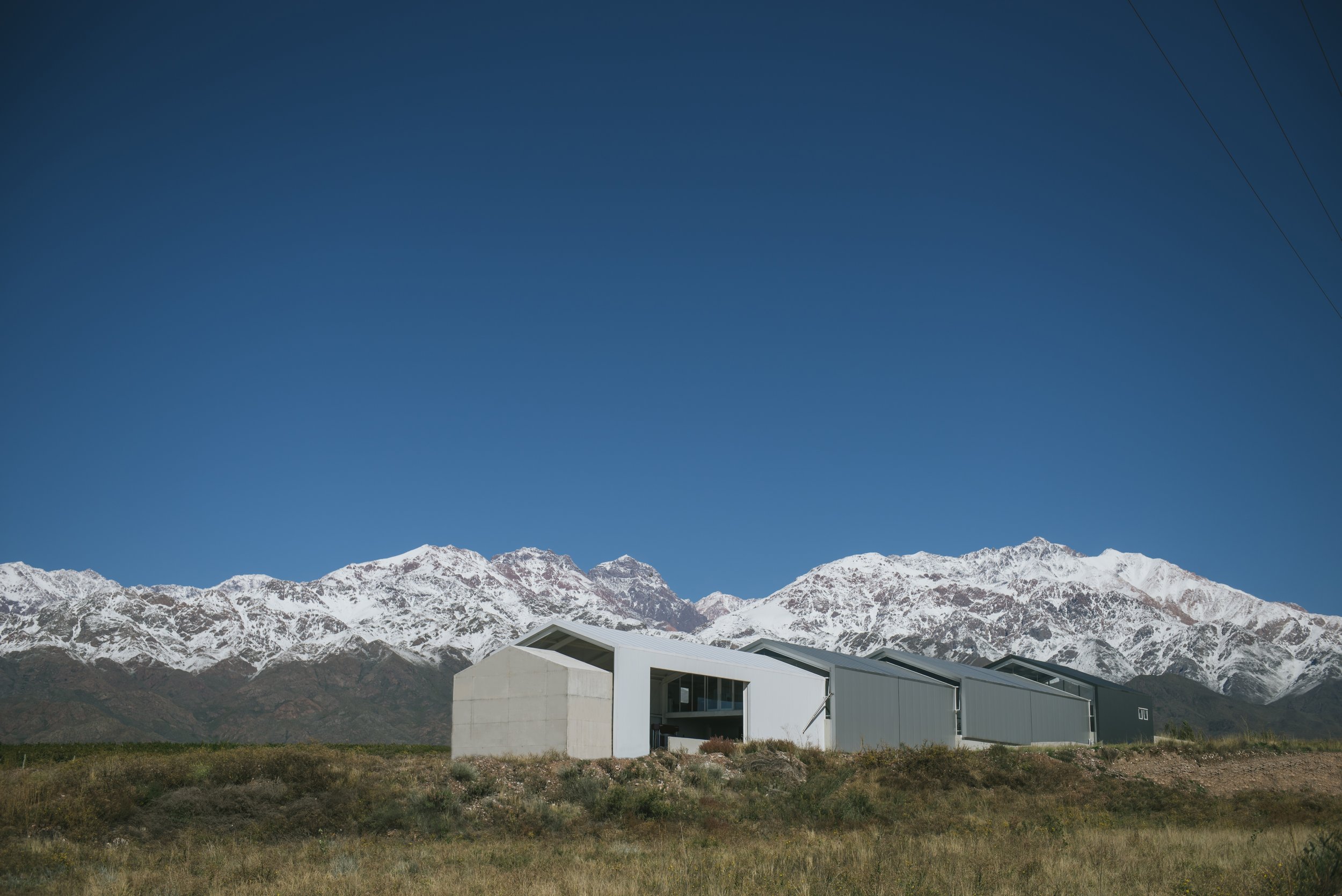 Edificio moderno de Casa de Uco con la cordillera de los Andes nevada al fondo bajo cielo despejado.