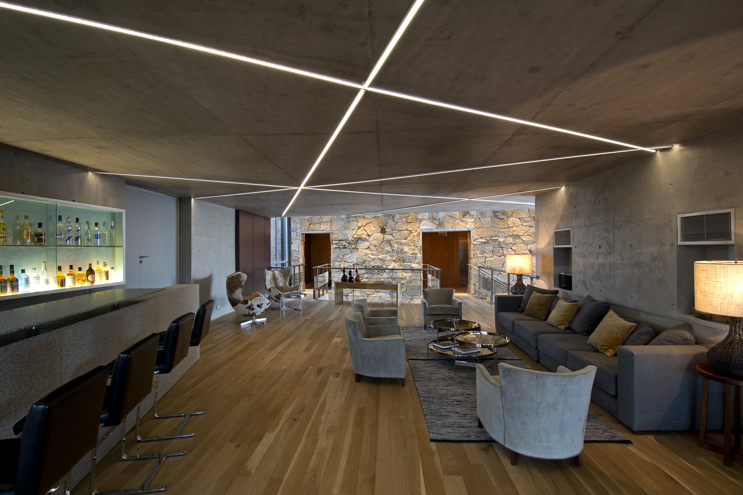 Salón común de un hotel con barra de bar, sillones modernos y paredes de hormigón visto y piedra