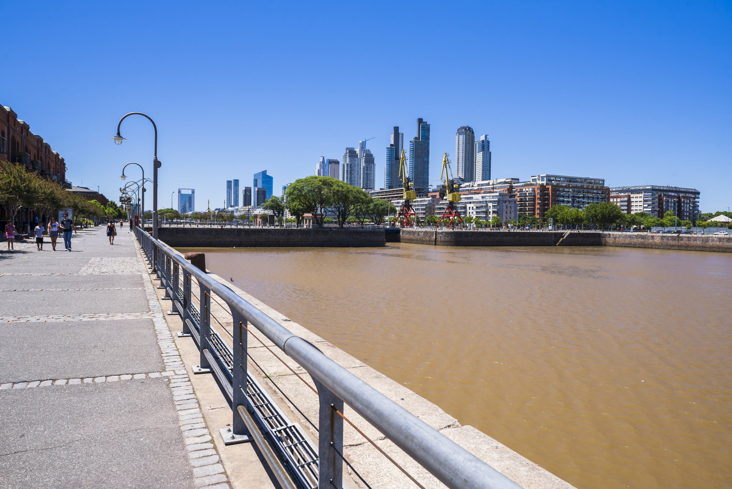 Vista panorámica del dique de Puerto Madero con sus grúas históricas, rambla peatonal y edificios modernos.