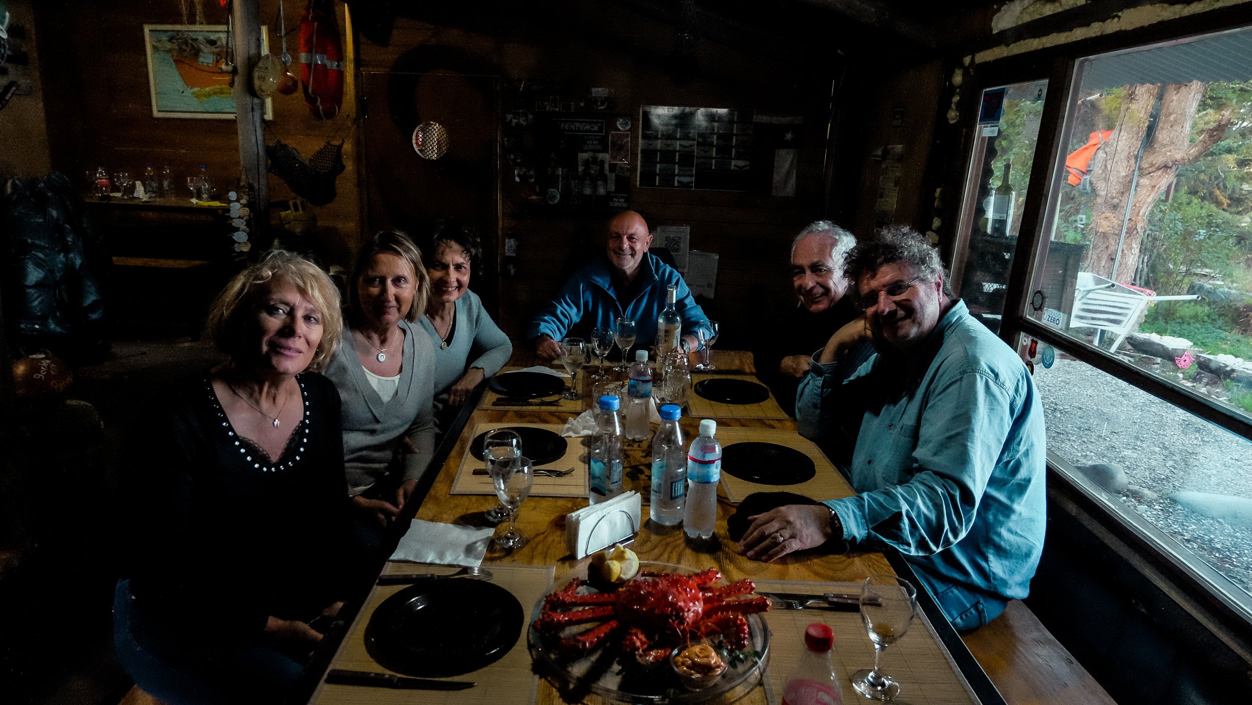 Grupo de comensales sentados a la mesa en un restaurante rústico a punto de comer centolla.