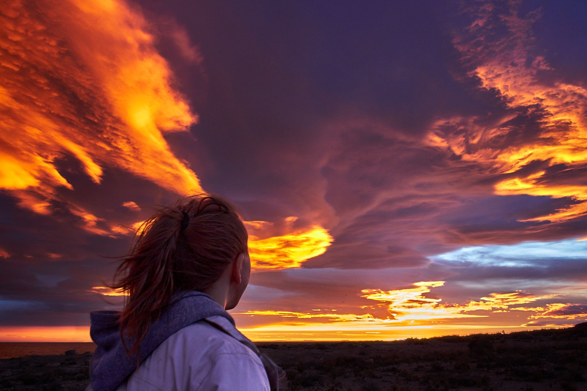 Persona de espaldas contemplando un cielo encendido por nubes rojizas durante el atardecer en la costa patagónica.