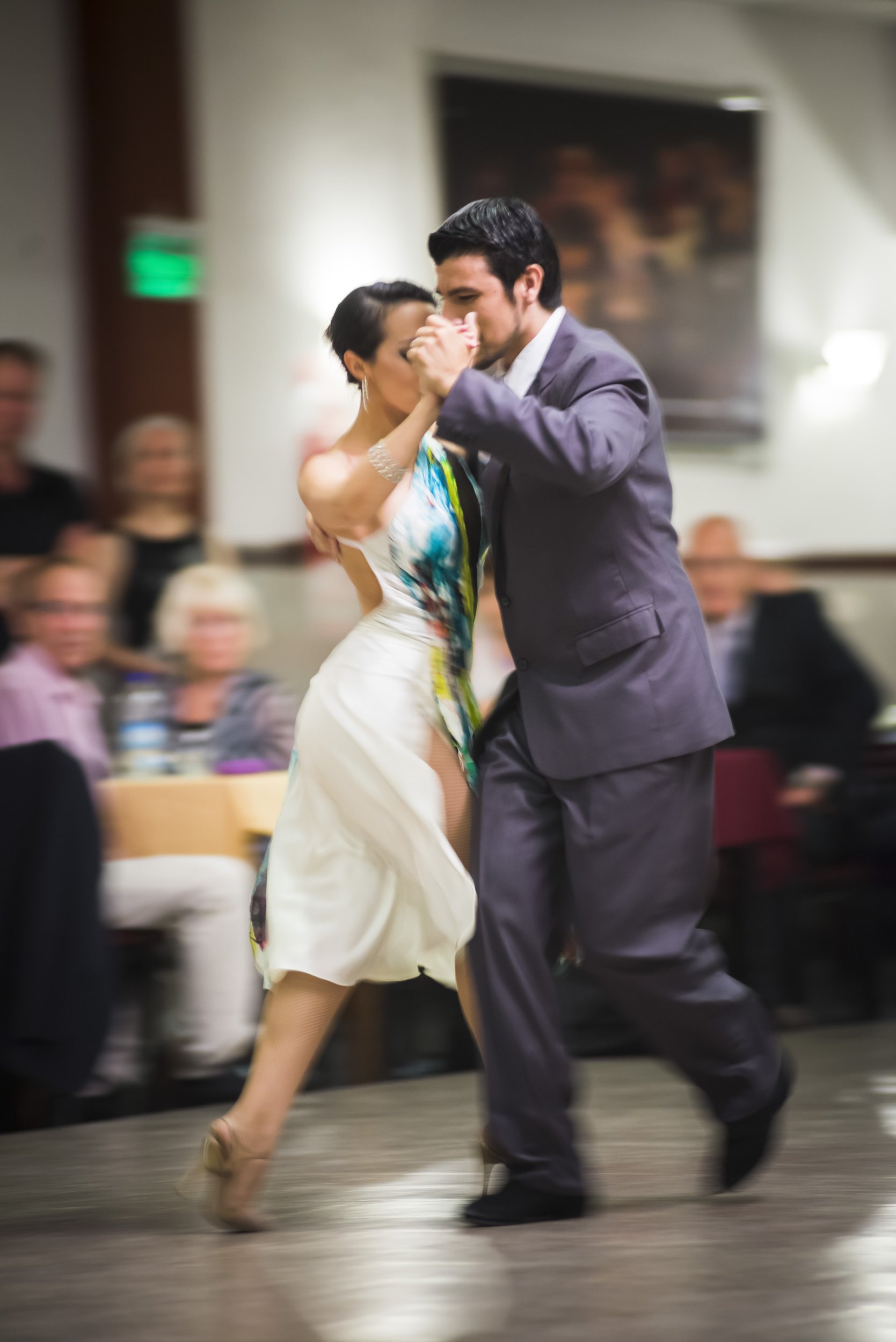 Pareja bailando tango en una pista de baile durante una milonga frente a los espectadores.