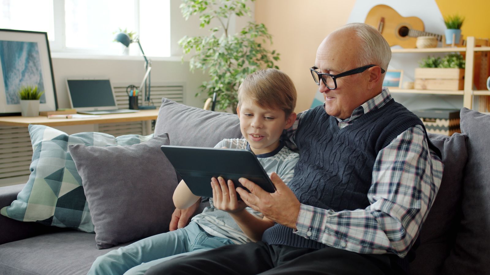 A grandfather and grandson sharing a tablet on a living room sofa