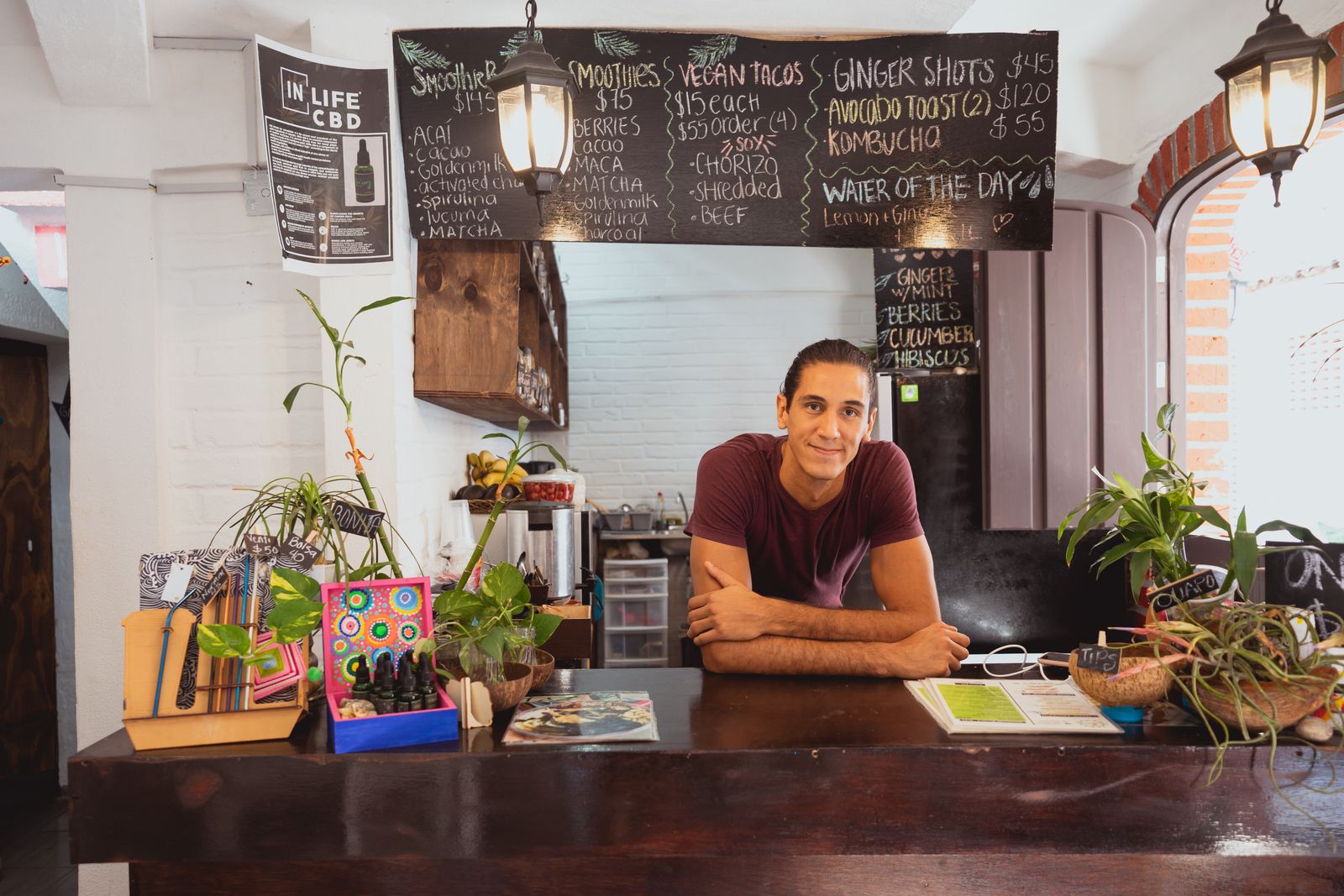 A smiling man behind the counter of a small cafe with a chalkboard menu