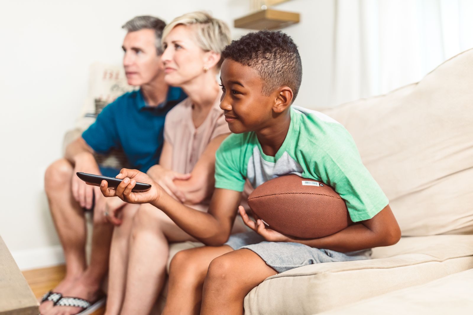 A family relaxing together on a sofa watching TV, one holding a phone