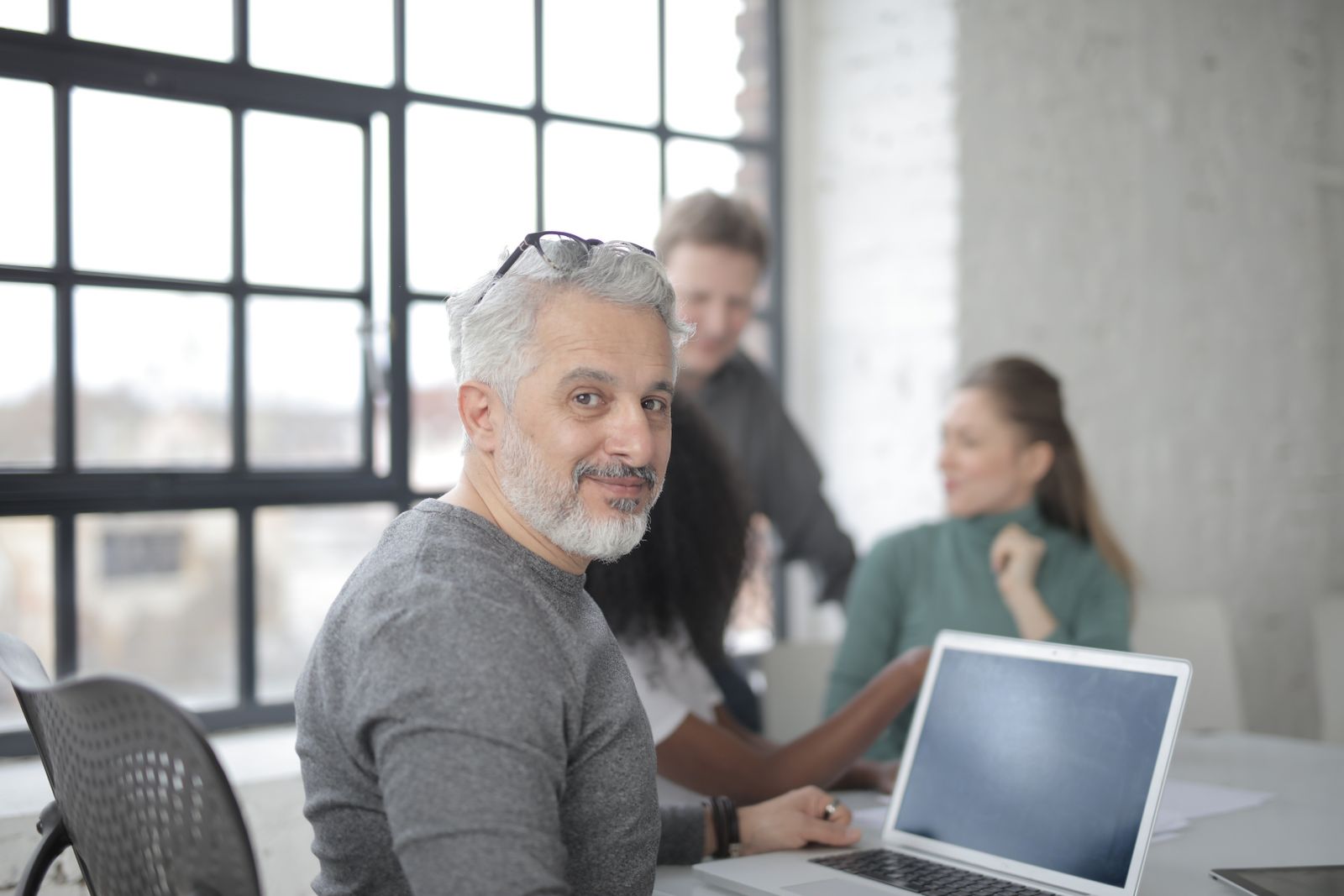 Coworkers gathered at a laptop in a bright office with large windows