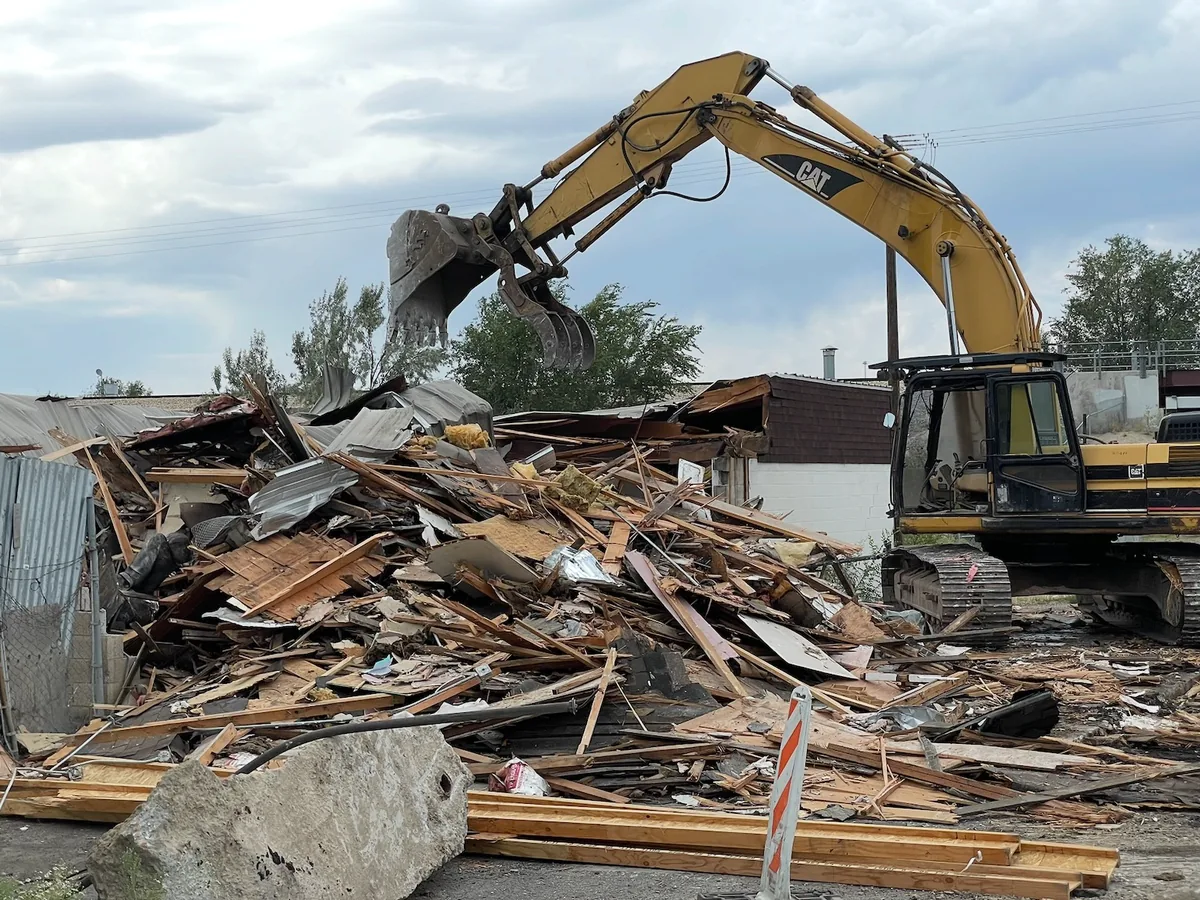 CAT excavator with a grapple tearing down a building beside a large debris pile, Ritz Excavation & Demolition