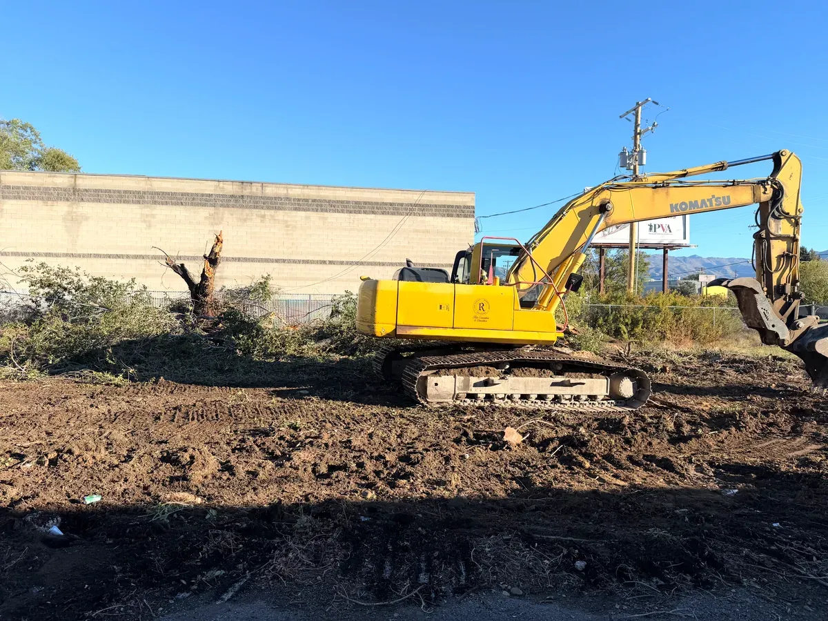 Komatsu excavator clearing trees and brush from a lot, leaving bare graded dirt