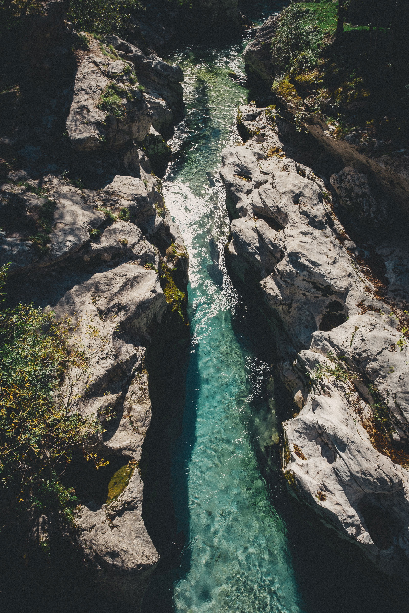 Clear turquoise river flowing through a narrow rocky gorge with large light gray rocks and some green vegetation on the sides.