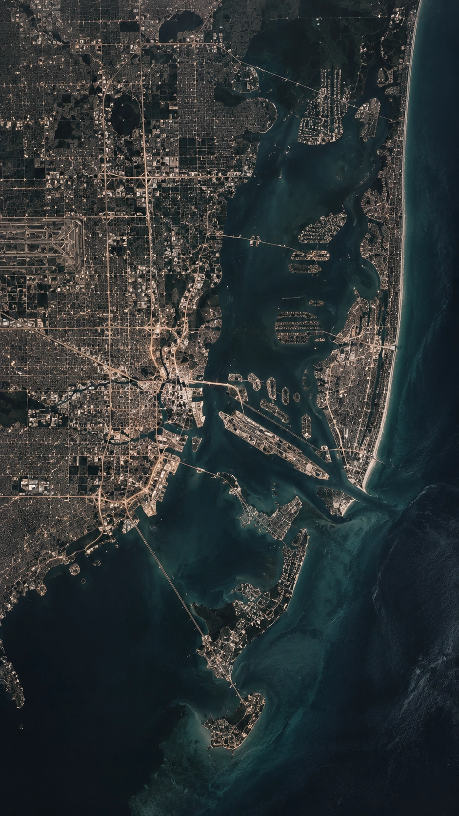 Aerial satellite view of Miami, Florida, showing urban areas, roads, waterways, several connected islands, and the coastline with visible beaches along the Atlantic Ocean.