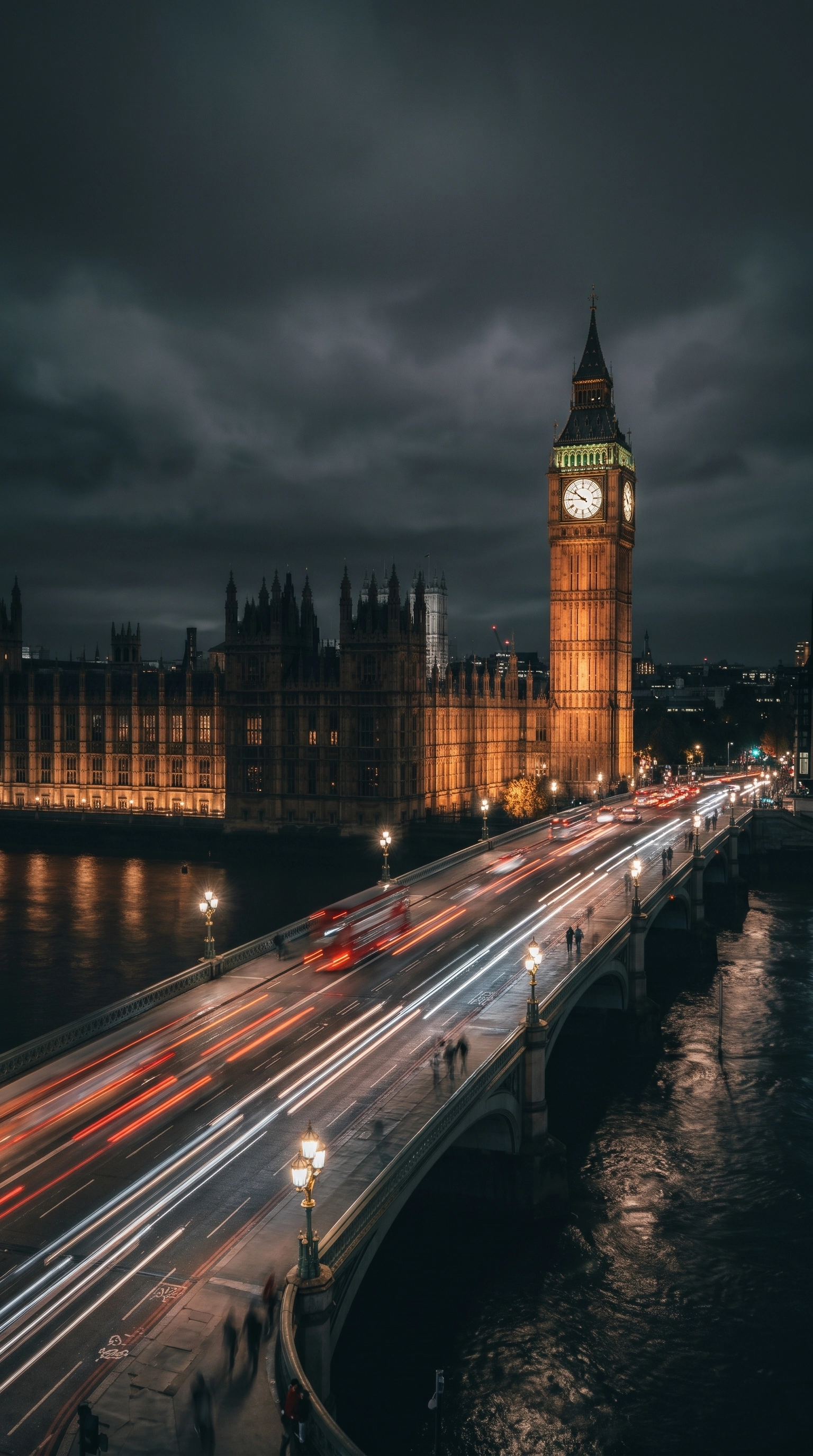 Night view of Westminster Bridge in London with light trails from vehicles crossing it, and the illuminated Big Ben clock tower and Houses of Parliament in the background under a cloudy sky.