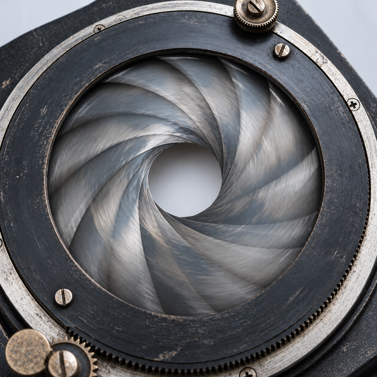 Close-up of a vintage camera shutter with overlapping metal blades forming a circular pattern around an open aperture, surrounded by a black metal ring with screws and small gears.