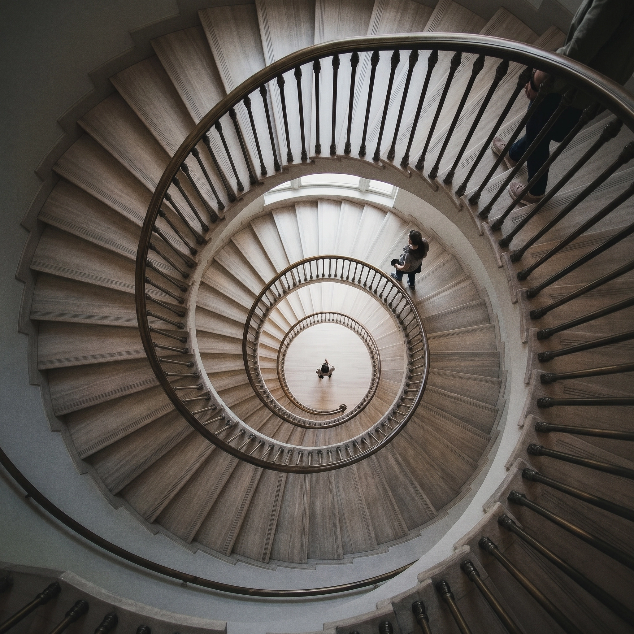 View from above of a spiraling wooden staircase with black metal railings and two people walking on the stairs.