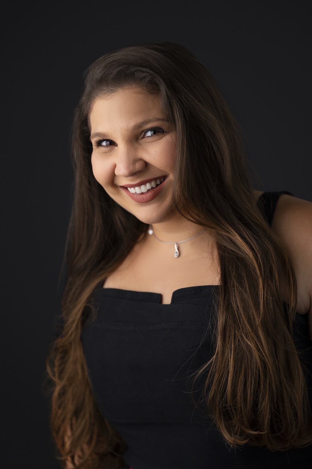 Professional headshot of a smiling woman with long brown hair on a dark background