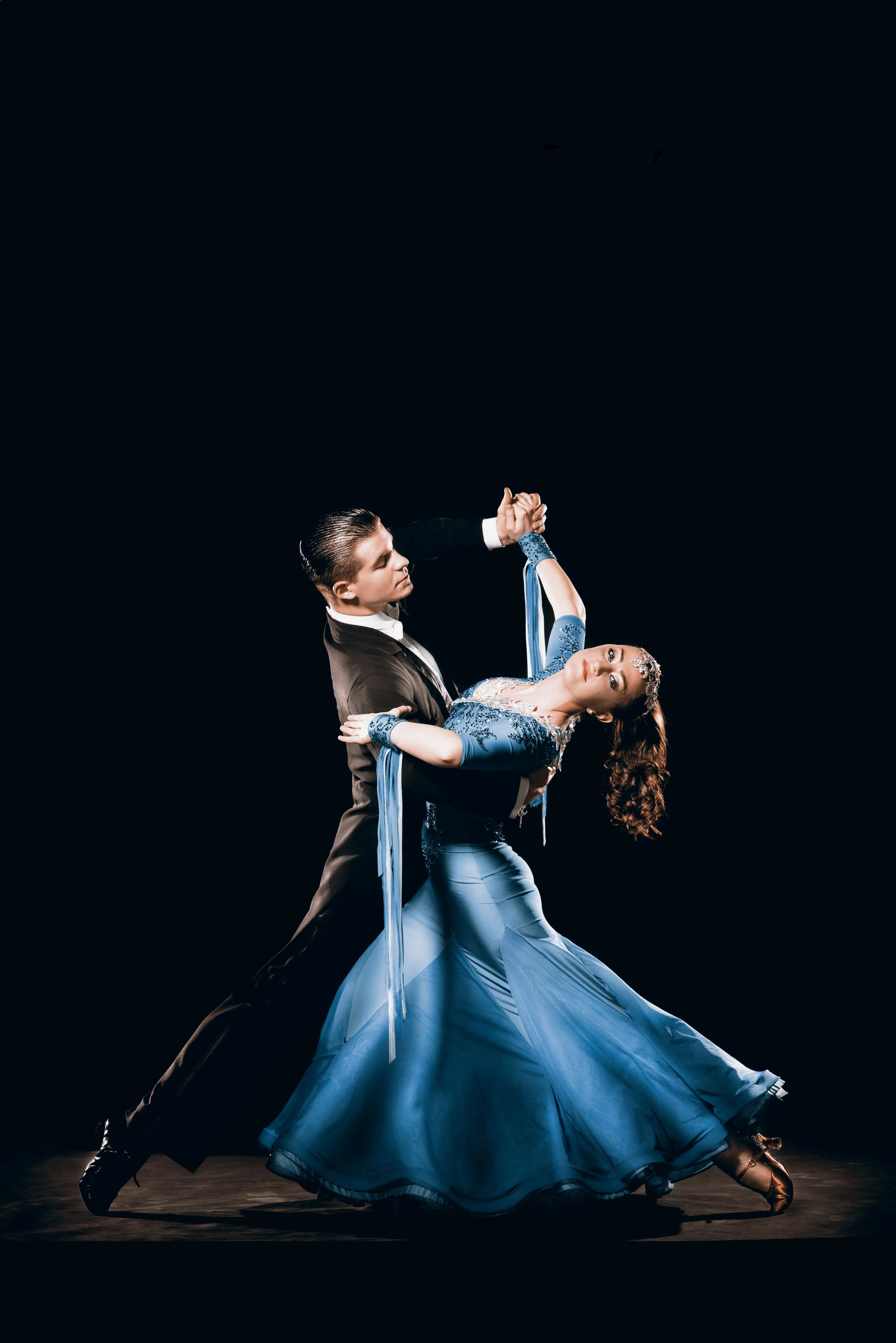 A ballroom partnership in a sweeping blue gown, connected through their raised hands.