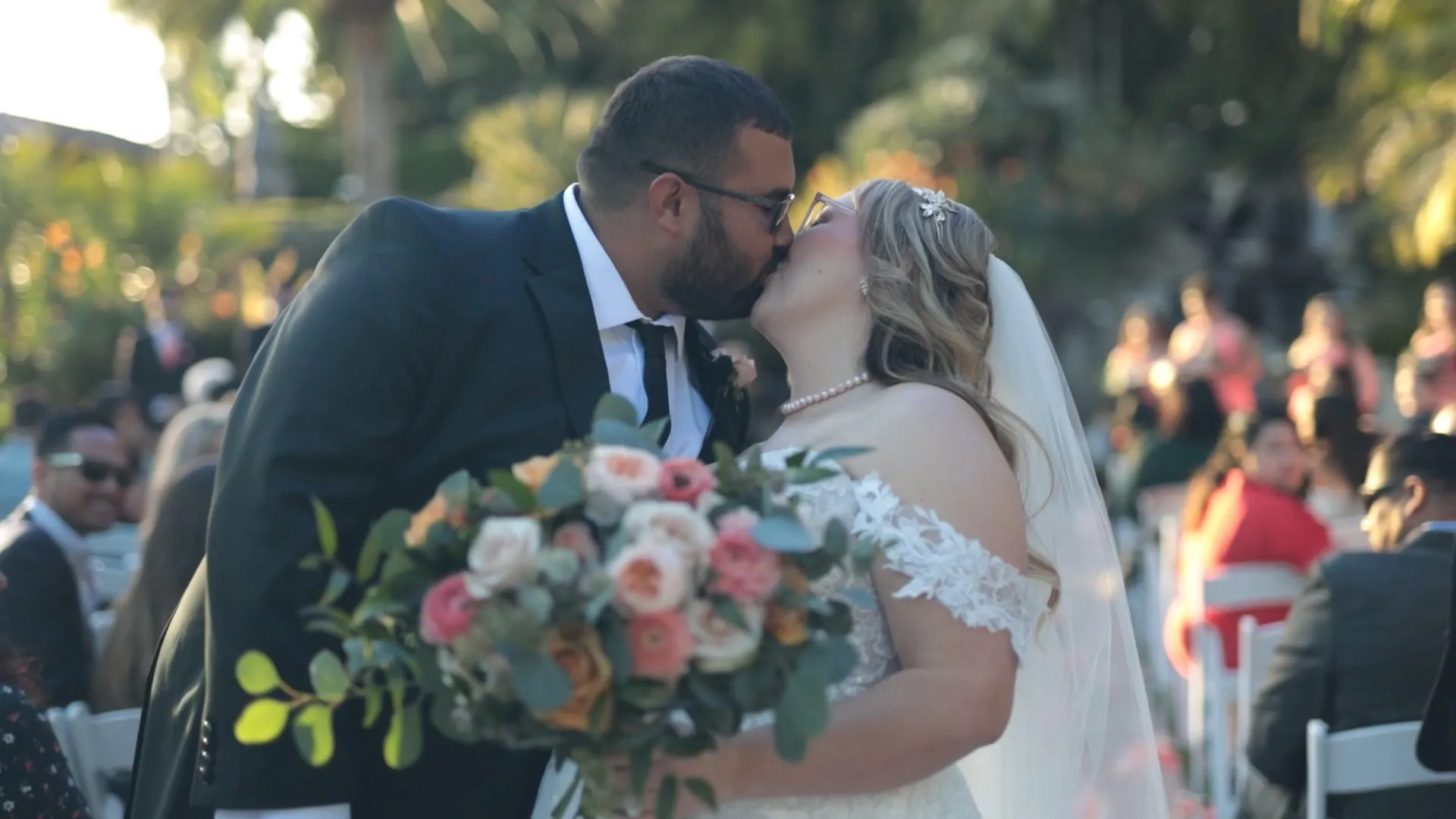 A bride holds her tearful groom close among deep green garden foliage.
