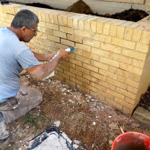 Mason repairing cracked mortar joints on a brick planter wall