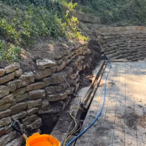 Boulderstone crew rebuilding a leaning stone retaining wall on a concrete block core