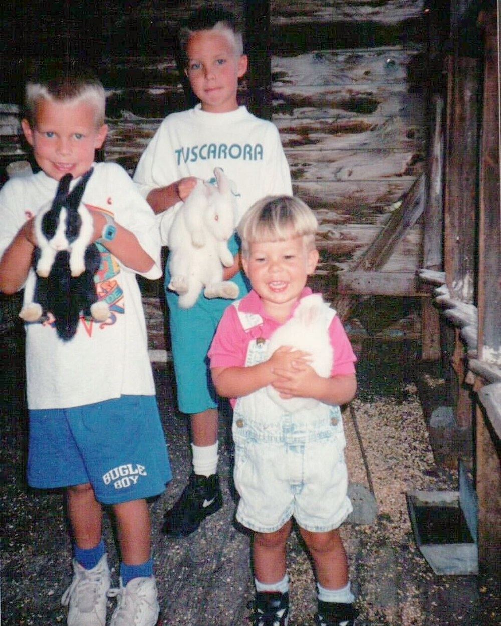 Three young brothers holding rabbits in a barn