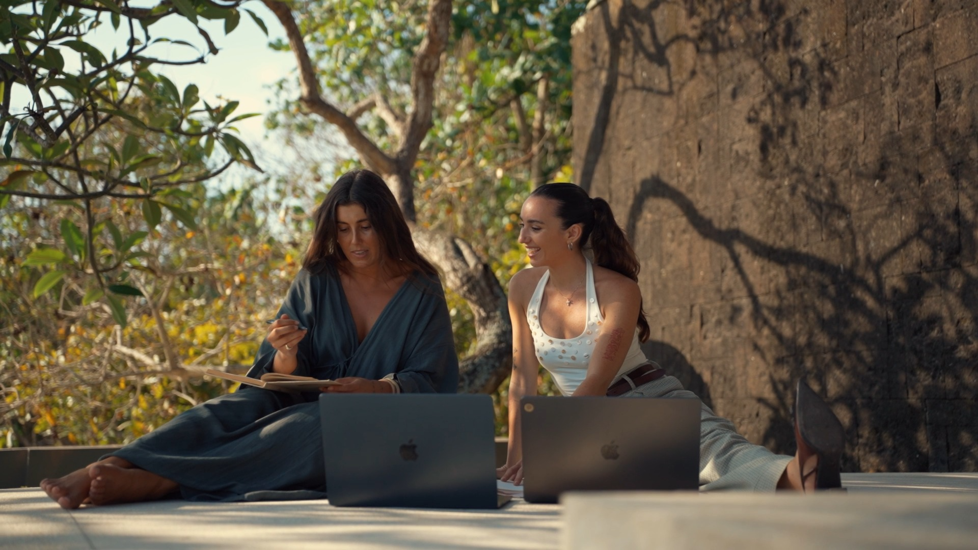 Two women sitting together outdoors in natural light with laptops