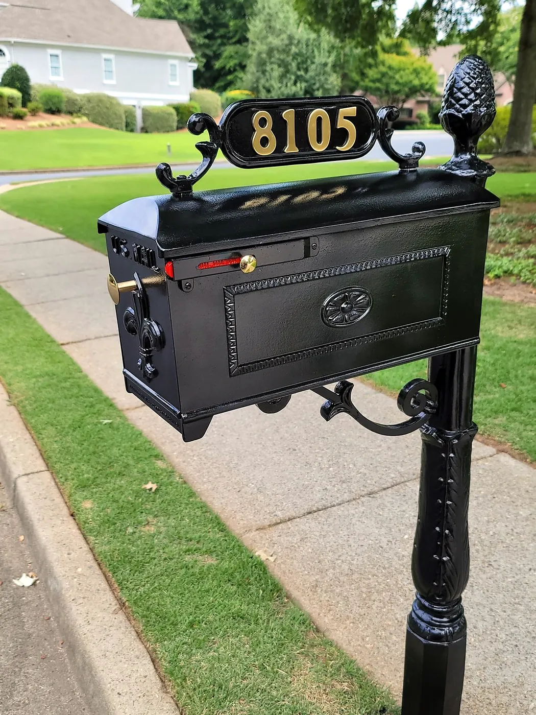 Black decorative mailbox with gold address numbers installed on a curbside post