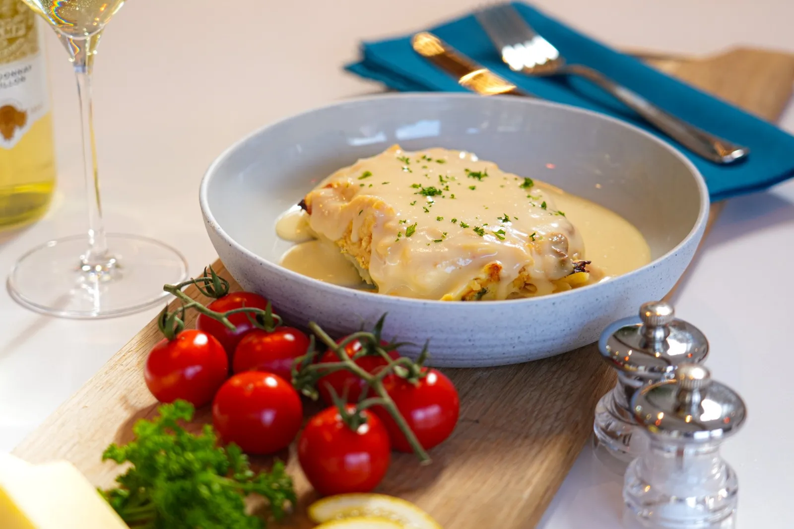 A fish dish in a cream sauce with vine tomatoes, parsley and a glass of white wine.