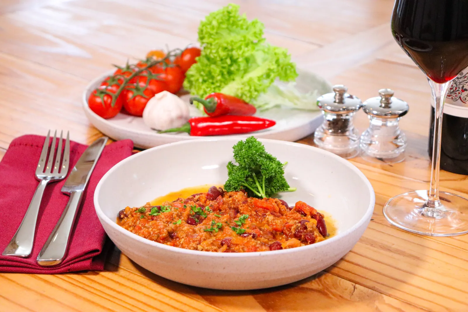 Chilli con carne in a stoneware bowl with fresh chillies, garlic, tomatoes and a glass of red wine.