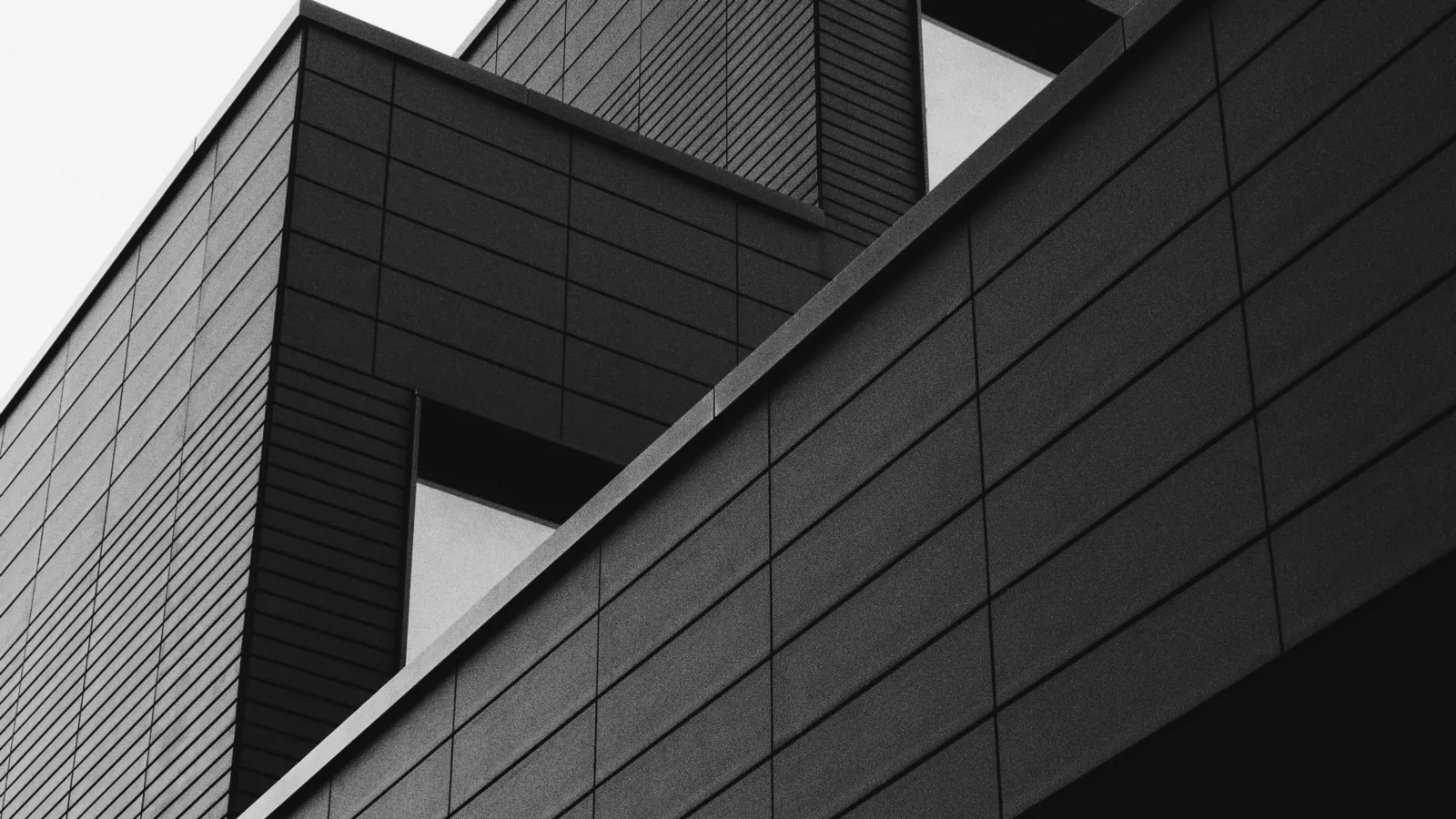 A modern building with dark ribbed cladding, photographed from below in black and white
