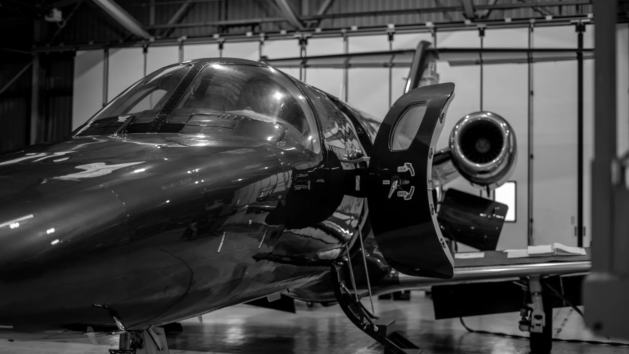 A light business jet in a hangar with its cabin door open, in black and white