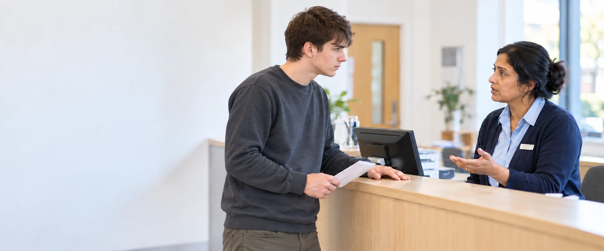 A young man discussing a letter with a receptionist at a front desk