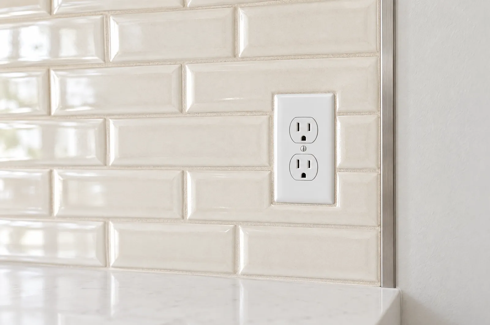 Close-up of a backsplash tile edge profile and an outlet set flush with the tile face