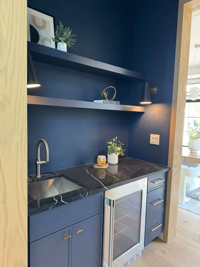 Navy blue wet bar cabinets with a black stone counter, an undercounter beverage fridge and an open shelf