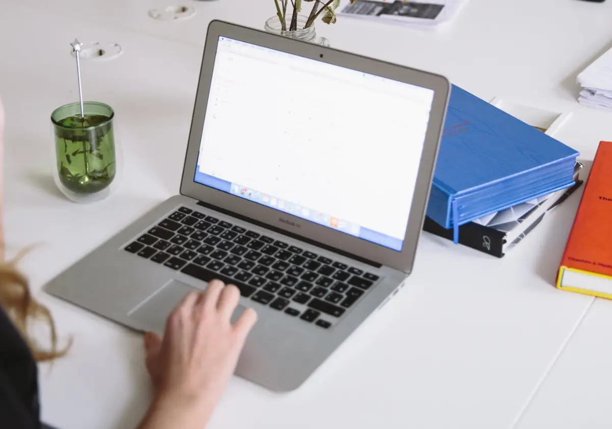 stock imagery of someone using laptop on white desk with peppermint tea and books strewn about
