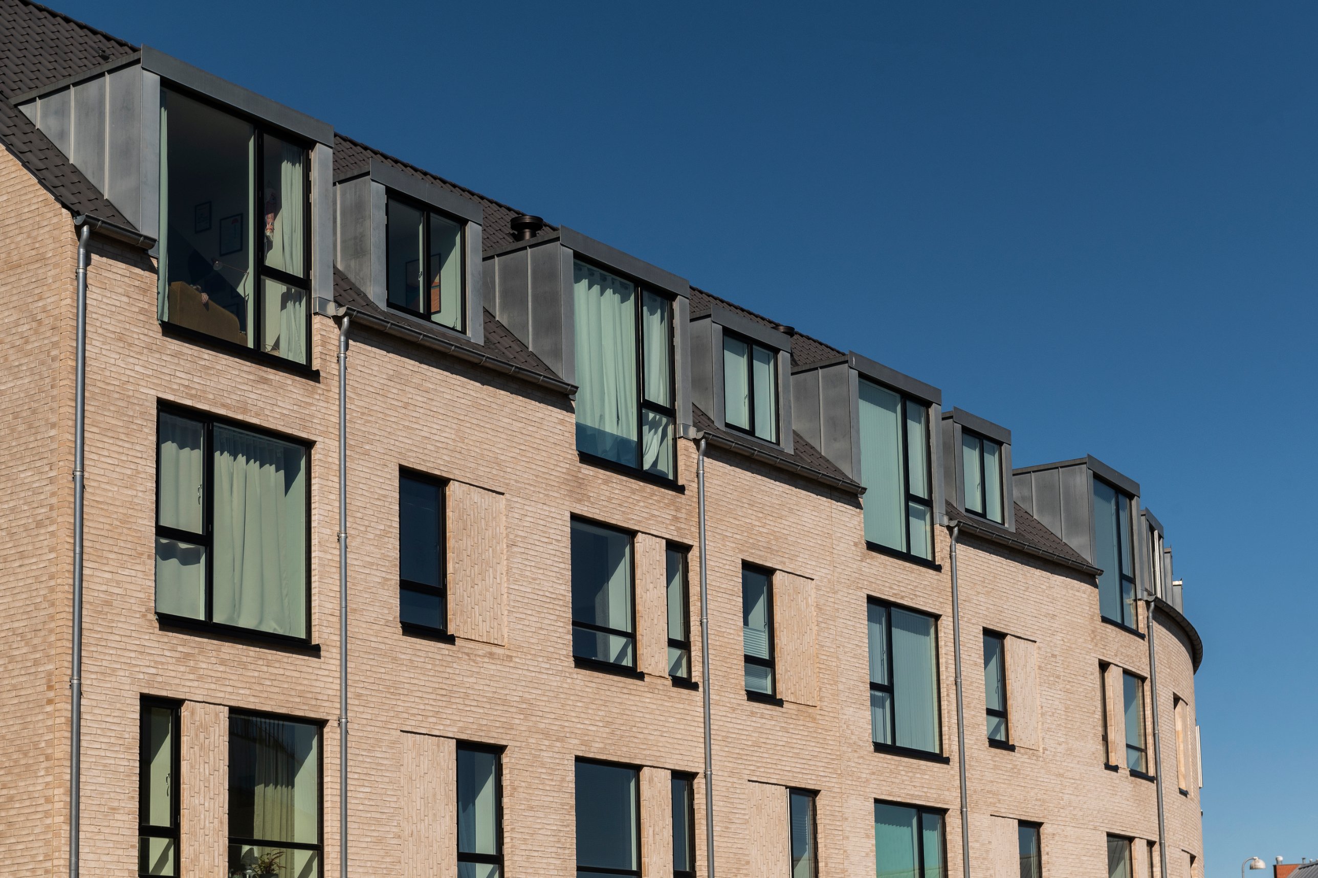 Facade af lejlighedsbyggeri i gule mursten med kviste mod blå himmel