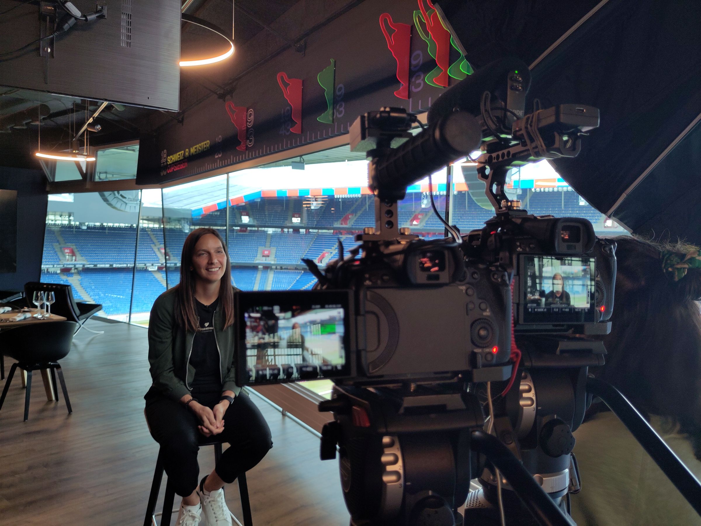 Interview vor einer Glasfront mit Blick in ein Fussballstadion